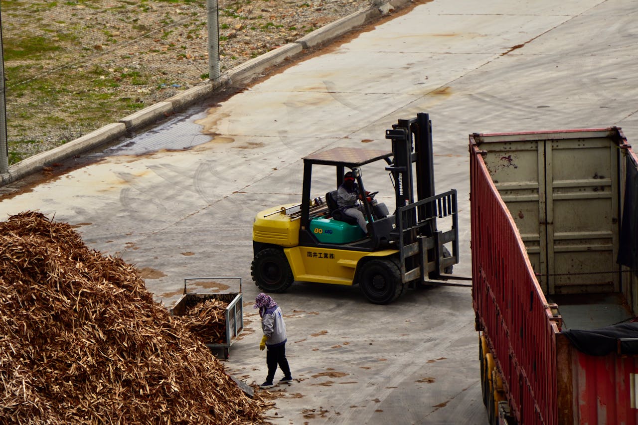 Forklift operator managing wood chips at an industrial lumber yard.